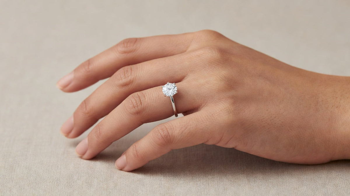 A 2 carat round moissanite solitaire ring worn on a hand showing how the stone spans the width of the finger