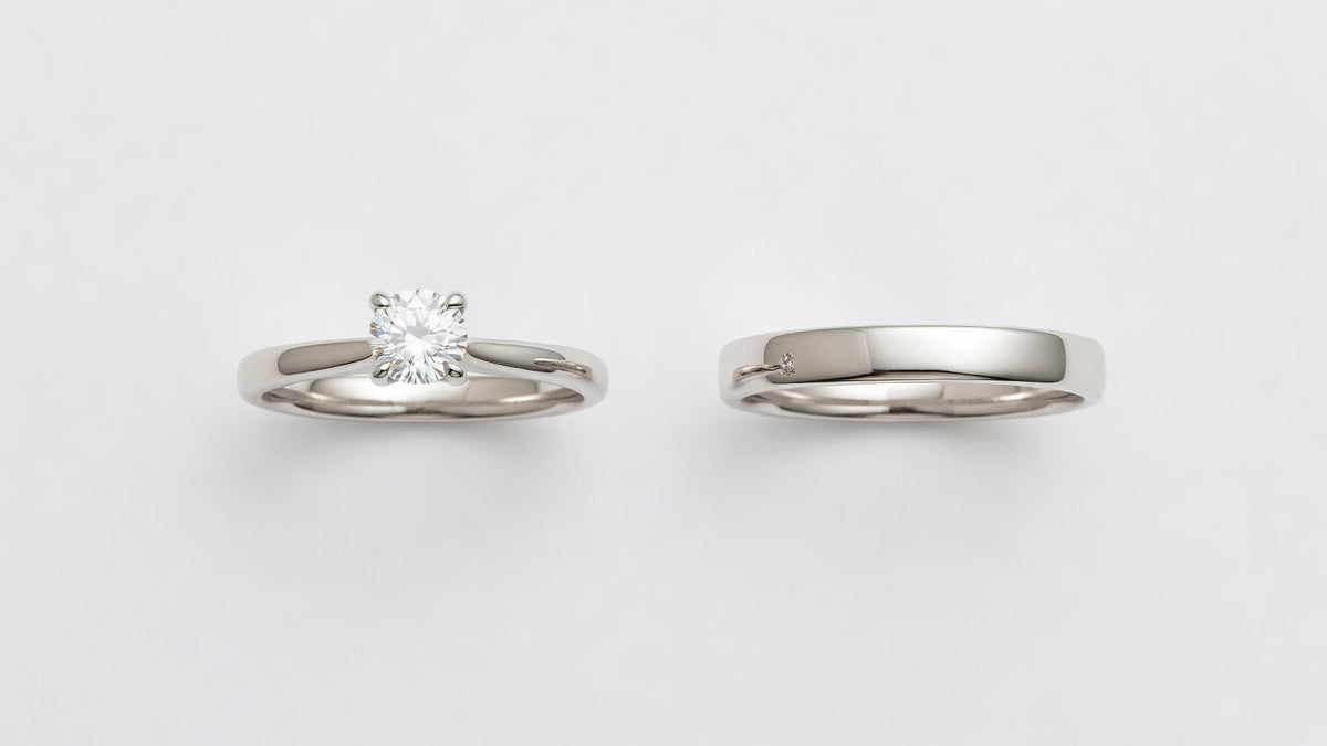 An engagement ring with a centre stone beside a plain wedding band on a white surface