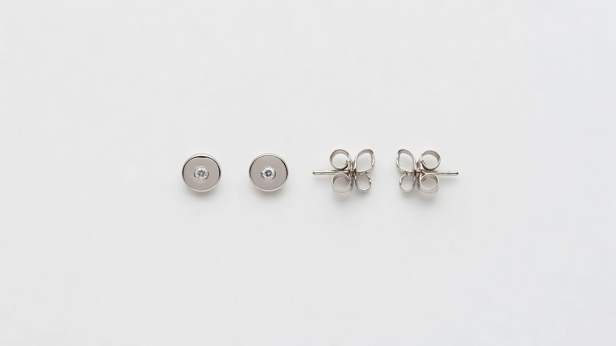 A pair of plain stud earrings with their backs beside them on a clean white surface