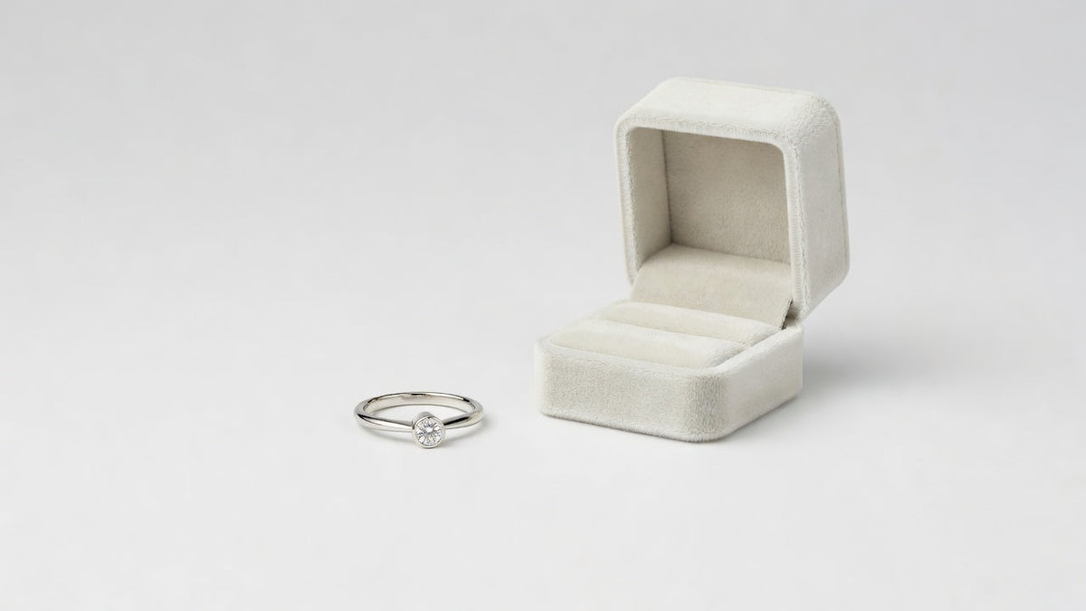 A slim moissanite promise ring in a low bezel setting photographed beside an open ring box on a white surface