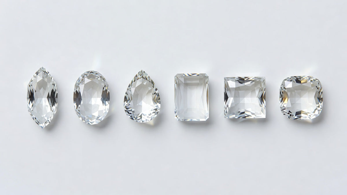 Six loose clear stones in different shapes arranged in a row on a white surface