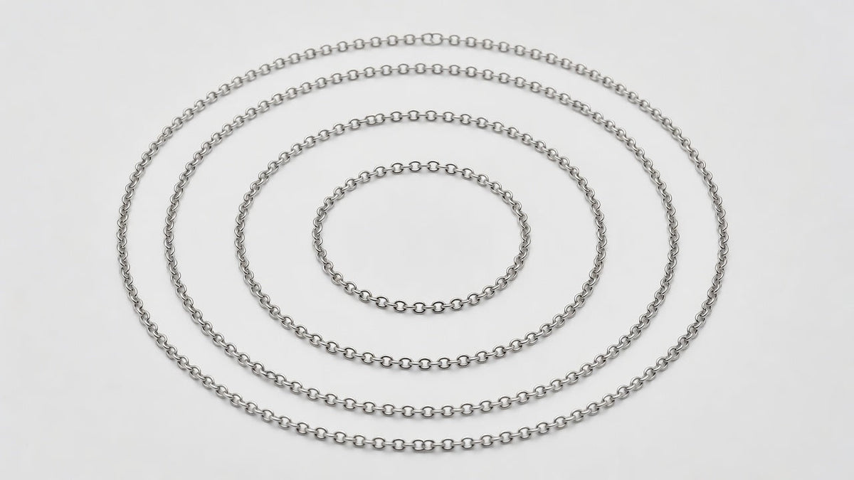 Several fine chain necklaces of increasing length laid out in concentric loops on a white surface