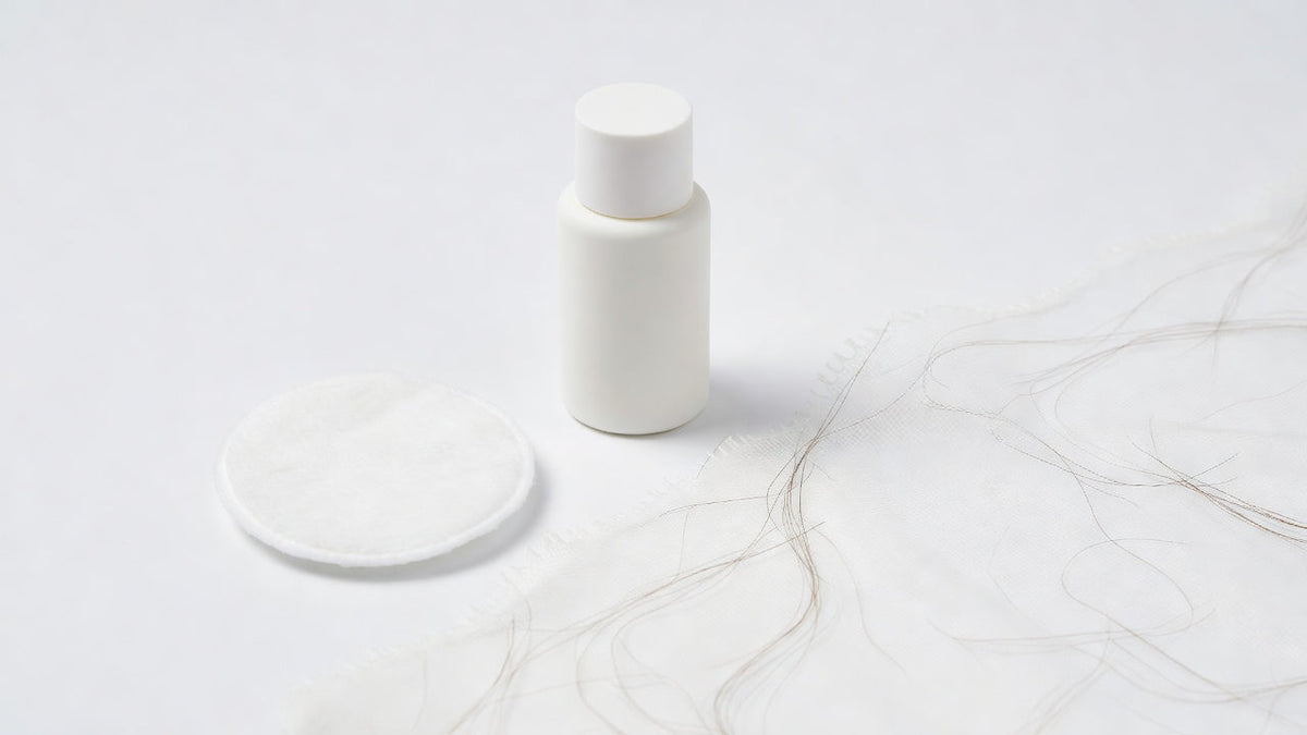 A bottle of adhesive remover and a cotton pad on a clean white surface beside a lace wig edge
